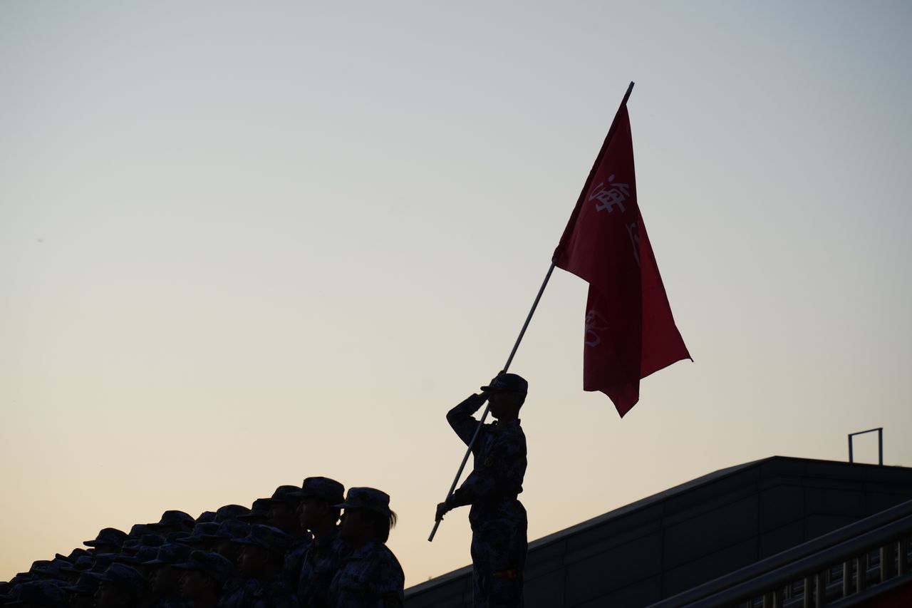 Silhouettes of soldiers standing before a large American flag at sunset